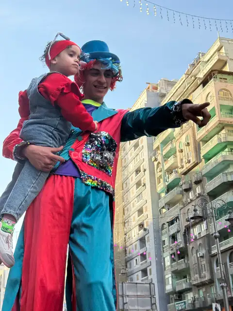 Clown on Stilts Carrying a Baby Girl on Eid Morning in Alexandria