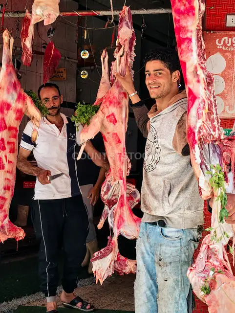 ضحكة جزارين جنب اللحمة المعلقة في السوق الشعبي