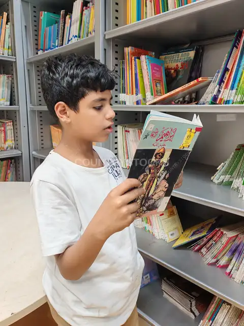 طفل يقرأ قصة مصورة بجوار أرفف المكتبة