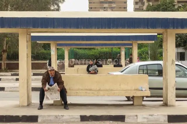 Man Sitting and Reading a Newspaper While Waiting for the Bus in Abbassia, Cairo
