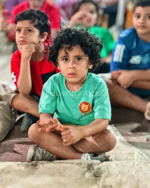 أطفال مصريون جالسون باهتمام في فعالية خارجية