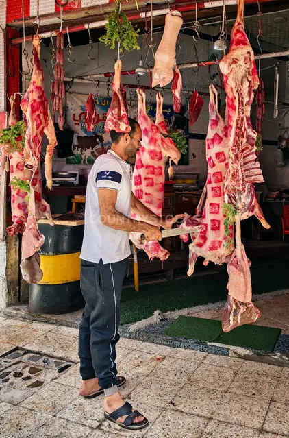 جزار مصري يقطع اللحوم المعلقة قبل عيد الأضحى