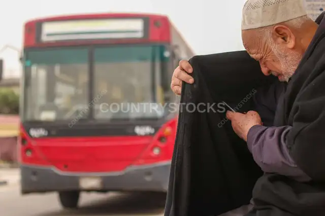 رجل مسن بيبص في موبايله بجانب أتوبيس المدينة