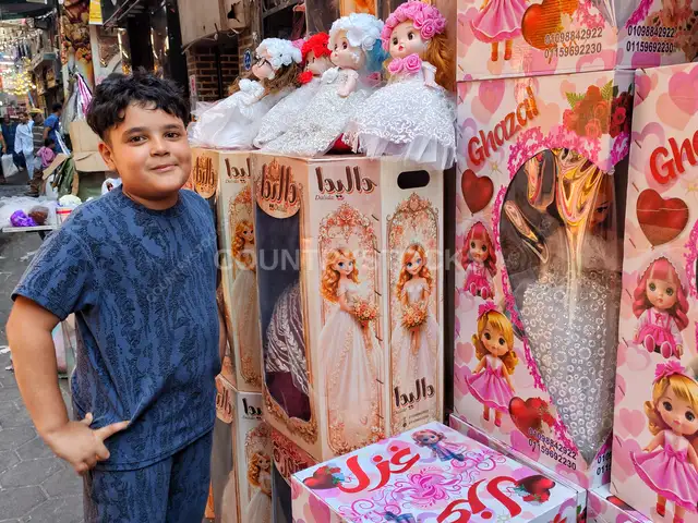 طفل يقف بابتسامة بجانب علب عرائس المولد بالسيدة زينب