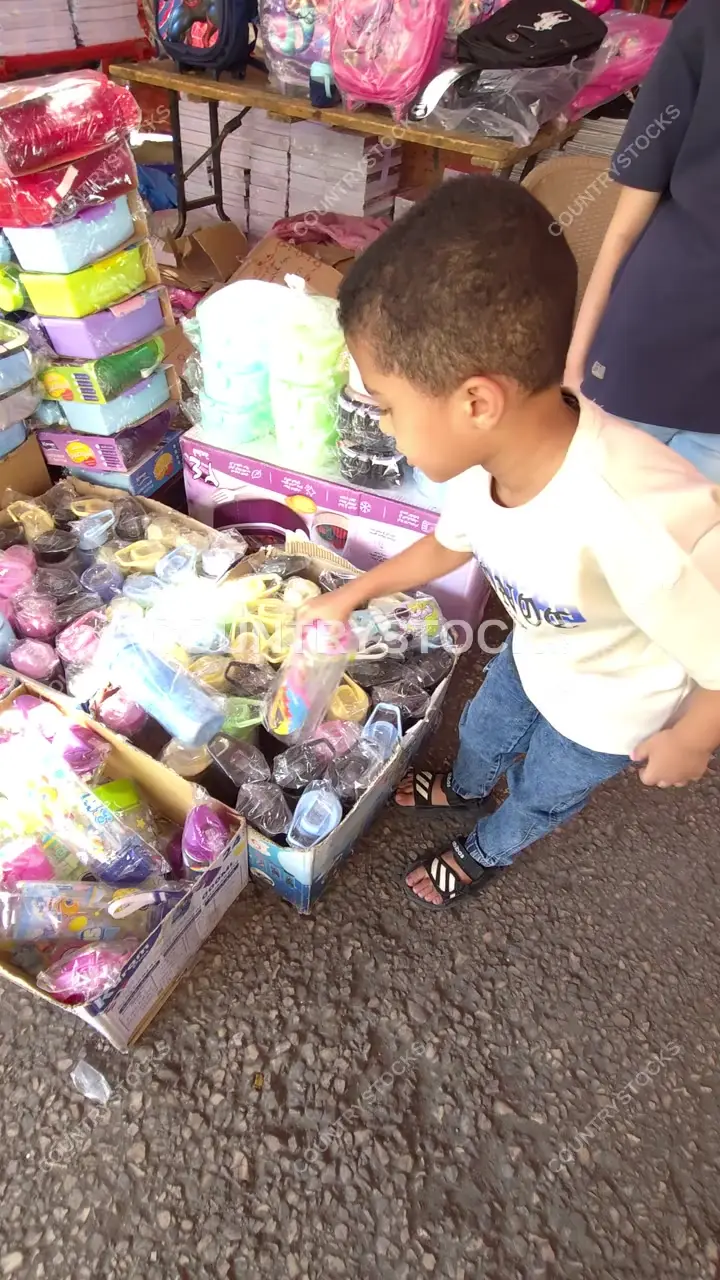 Child Selecting Water Bottle at Street Market, Abbasiya