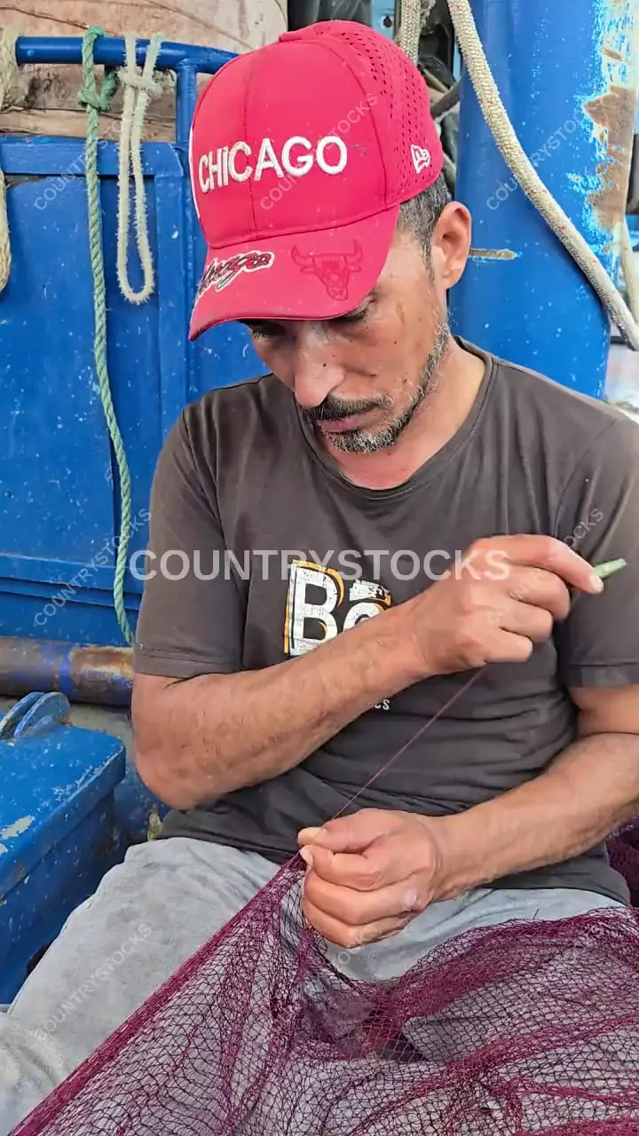 صياد مصري يرقع الشبكة على متن قارب صيد